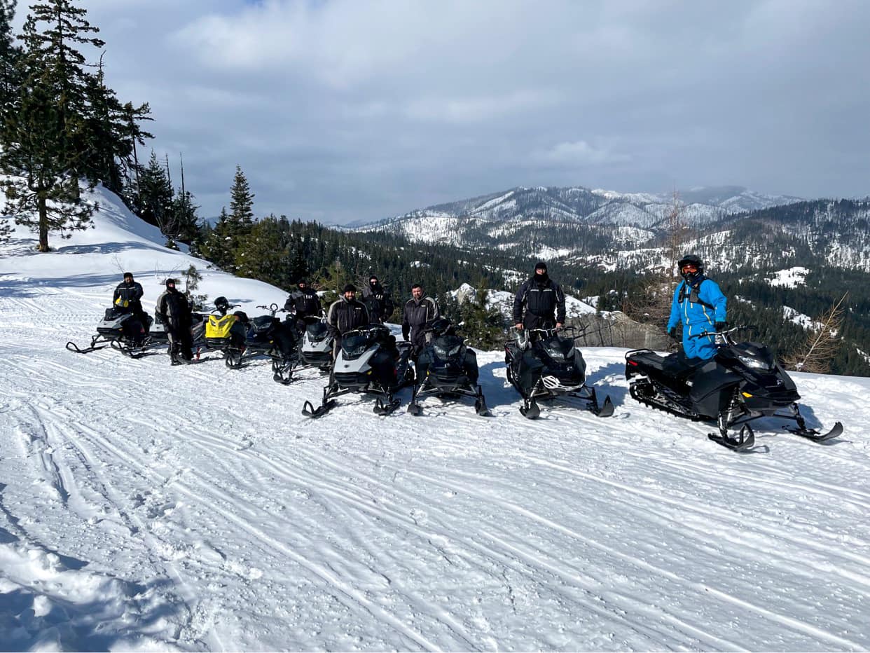 Group riding snowmobiles on snowy mountain terrain.