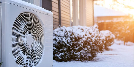 Snow-covered outdoor heat pump near house