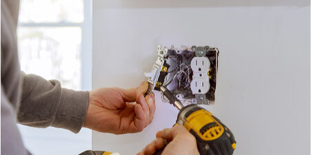 Electrician installing power outlet with drill