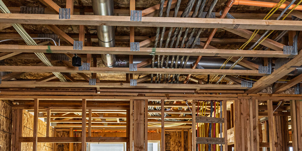 Wooden framing with plumbing and electrical wiring in progress.